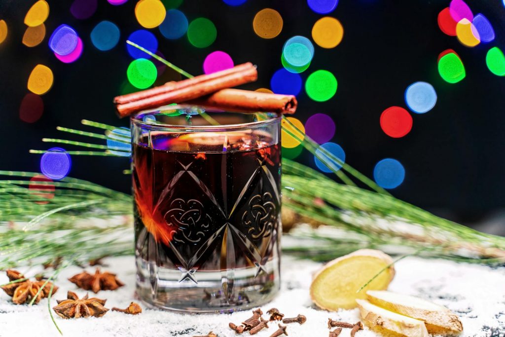 Decorative holiday cocktail with cinnamon sticks, surrounded by festive bokeh lights and spices.